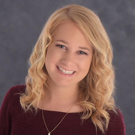 A close up photo of a smiling woman with blond wavy hair and a red sweater.